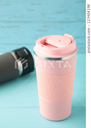 Two thermo cups or thermos mugs for tea or coffee on blue wooden background. Black and pink for him and her. Hot beverage for couples Two thermo cups or thermos mugs for tea or coffee on blue wooden background. Black and pink for him and her. Hot beverage for couples 123404196