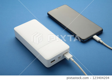 White powerbank charges smartphone on blue background. 123404204