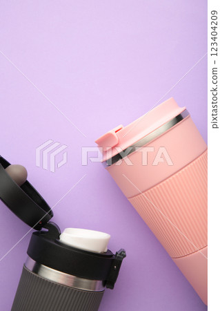 Two thermo cups or thermos mugs for tea or coffee on purple background. Black and pink for him and her. Hot beverage for couples 123404209