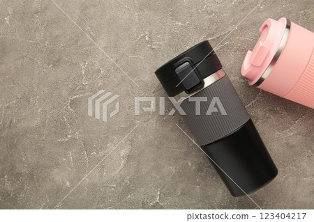 Two thermo cups or thermos mugs for tea or coffee on grey background. Black and pink for him and her. Hot beverage for couples Two thermo cups or thermos mugs for tea or coffee on grey background. Black and pink for him and her. Hot beverage for couples 123404217