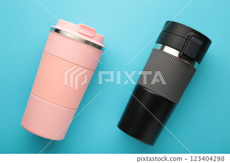 Two thermo cups or thermos mugs for tea or coffee on blue background. Black and pink for him and her. Hot beverage for couples Two thermo cups or thermos mugs for tea or coffee on blue background. Black and pink for him and her. Hot beverage for couples 123404298