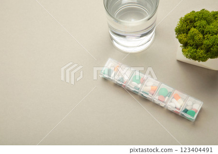 Pill box with medicaments and glass of water on grey background. Space for text 123404491