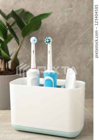 Holder with modern electric toothbrushes and plant on blue background Holder with modern electric toothbrushes and plant on blue background 123404585