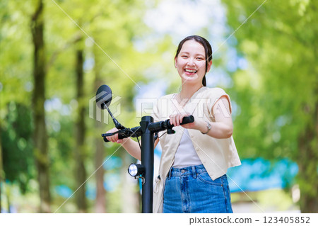 A young woman running on a tree-lined street with an electric kickboard 123405852