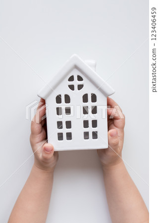 Child hands holding ceramic house model against white background 123406459