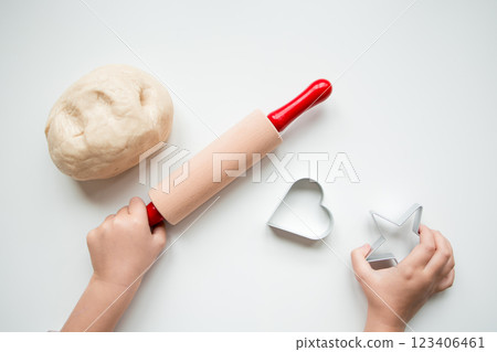Child hands using rolling pin and cookie cutters for baking on white surface 123406461