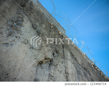 old decayed concrete wall with barbwire on top with blue sky above old decayed concrete wall with barbwire on top with blue sky above 123406714