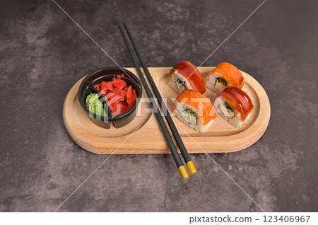 Set of sushi roll with rice and fish, wasabi, ginger and chopsticks on wooden serving board. Dark black texture background with copy space. Japan menu. Asian Set of sushi roll with rice and fish, wasabi, ginger and chopsticks on wooden serving board. Dark black texture background with copy space. Japan menu. Asian 123406967