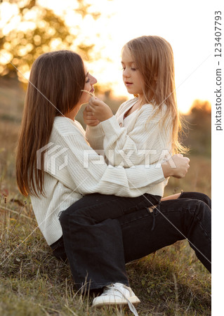 Family day, mother's day. Happy smiling young mom and adorable child daughter soft hugging, kissing and spending time together at autumn on sunset. Idyllic family having fun outdoors on fall holiday. Family day, mother's day. Happy smiling young mom and adorable child daughter soft hugging, kissing and spending time together at autumn on sunset. Idyllic family having fun outdoors on fall holiday. 123407793