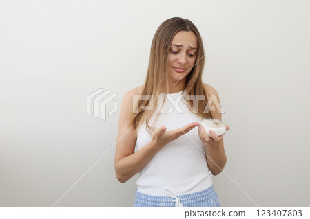 Frustrated young woman with hair loss problem holds hair brush and shows on bunch of fallen hair after combing. Alopecia, endocrine disorder, hormonal imbalance, postpartum period, stress concept 123407803