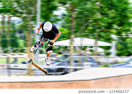 Young man practicing Scootering (Freestyle Scootering) in the new SkatePark in the central park of Igualada, Barcelona, Spain. blurred background 123408257
