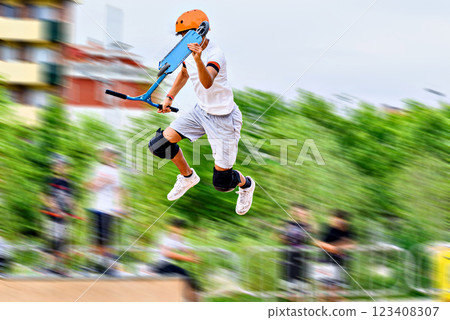 Young man practicing Scootering (Freestyle Scootering) in the new SkatePark in the central park of Igualada, Barcelona, Spain. blurred background 123408307