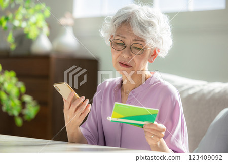 Senior woman looking at smartphone and bankbook worried 123409092