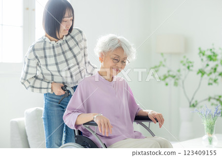 A grandmother in a wheelchair and her granddaughter spending time together in the living room 123409155