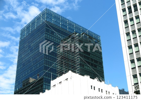 A high-rise building with a glass curtain wall, with the neighboring building reflected in its surface 123411175