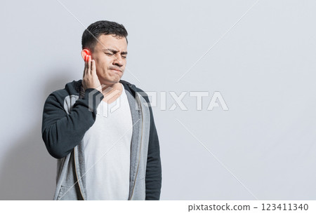 Person with ear pain, on isolated background, Suffering man massaging his ear isolated, A person with otitis and tinnitus Person with ear pain, on isolated background, Suffering man massaging his ear isolated, A person with otitis and tinnitus 123411340