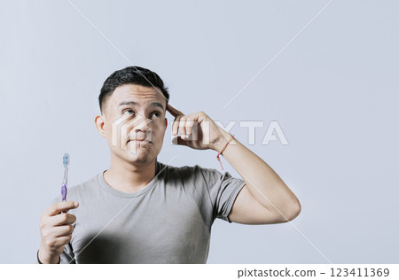 Man holding toothbrush with pensive expression isolated. Person holding toothbrush looking up, Thoughtful man holding toothbrush isolated, Portrait of young man thinking holding toothbrush Man holding toothbrush with pensive expression isolated. Person holding toothbrush looking up, Thoughtful man holding toothbrush isolated, Portrait of young man thinking holding toothbrush 123411369