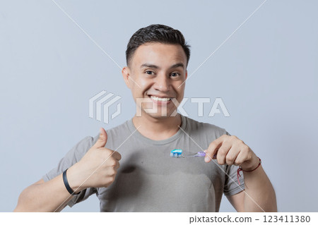 Smiling handsome guy holding a toothbrush with thumb up. Smiling people holding toothbrush with thumbs up gesture, Young man holding a toothbrush with thumb up isolated Smiling handsome guy holding a toothbrush with thumb up. Smiling people holding toothbrush with thumbs up gesture, Young man holding a toothbrush with thumb up isolated 123411380