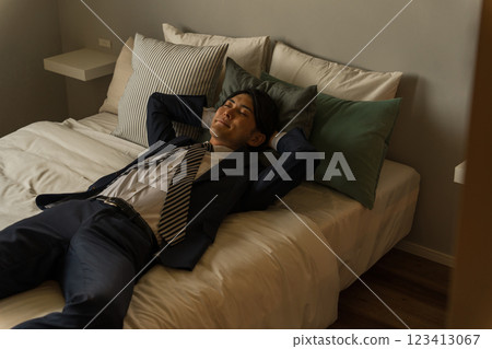 一位年輕的亞洲男商人回家後穿著西裝躺在床上 一位年輕的亞洲男商人回家後穿著西裝躺在床上 123413067
