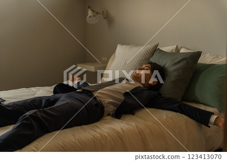一位年輕的亞洲男商人回家後穿著西裝躺在床上 一位年輕的亞洲男商人回家後穿著西裝躺在床上 123413070