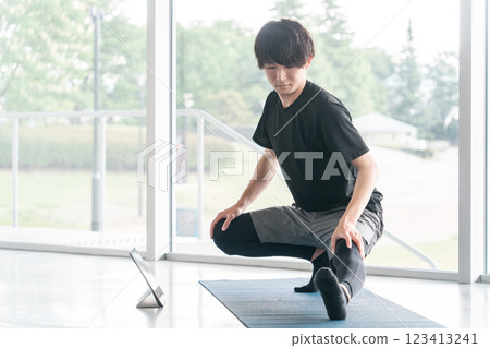 A young Asian man bending and stretching while watching a training video on a computer 123413241