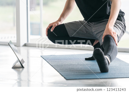 A young Asian man bending and stretching while watching a training video on a tablet 123413243