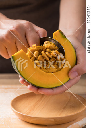 Hand holding spoon and removing seeds from pumpkin, Homemade cooking Hand holding spoon and removing seeds from pumpkin, Homemade cooking 123413724