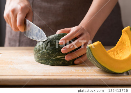Hand holding kitchen knife and cutting green pumpkin on wooden board, Homemade cooking Hand holding kitchen knife and cutting green pumpkin on wooden board, Homemade cooking 123413726
