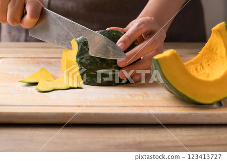 Hand holding kitchen knife and cutting green pumpkin on wooden board, Homemade cooking 123413727