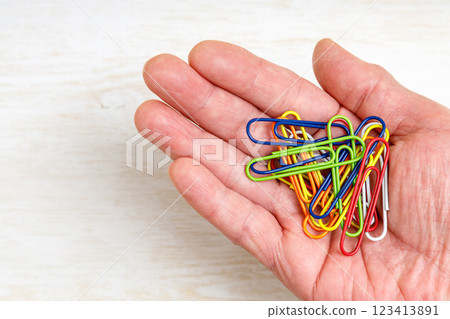 Paper clip in right hand | Wood grain background 123413891