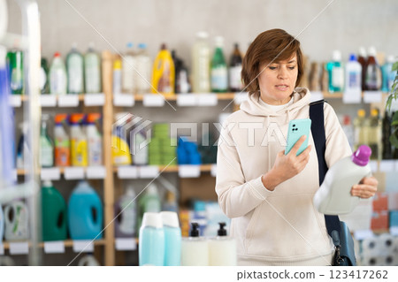 Woman client scans QR code on package and downloads promo code to purchase liquid detergent Woman client scans QR code on package and downloads promo code to purchase liquid detergent 123417262