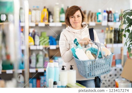 Woman with filled basket wanders around store, looking at display cases and inspects assortment 123417274
