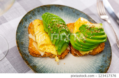 Hearty sandwich with toast, cheese, plate of egg omelet and pieces of avocado. Hearty sandwich with toast, cheese, plate of egg omelet and pieces of avocado. 123417376
