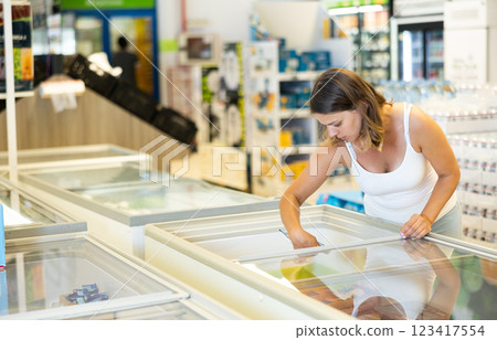 Woman buyer carefully chooses frozen food in store freezer Woman buyer carefully chooses frozen food in store freezer 123417554