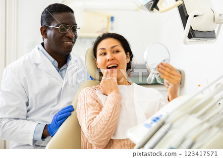 Dentist patient looks in the mirror at new tooth after surgery 123417571