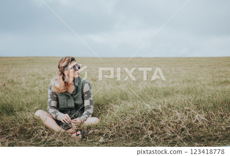 Portrait of girl in glasses sitting cross legged in the field. Relaxed teen girl sitting in the field looking to the side. Concept of young woman sitting and relaxing in the field 123418778
