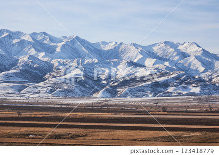 Spring natural landscape Kyrgyzstan. Plowed fields and snow-capped mountains. Preparing the soil for the sowing season 123418779