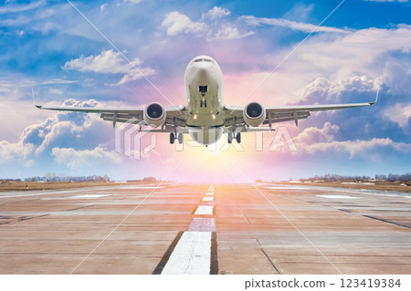 White passenger airplane take off from airport runway against the backdrop of a picturesque evening sky with sun rays 123419384