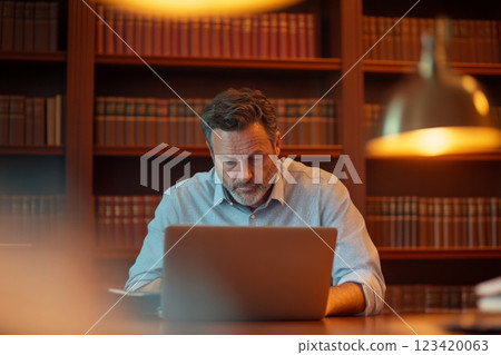 Lawyer working at desk with laptop and surrounded by legal books in office 123420063