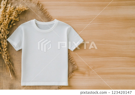 Minimalist photo of a blank white t-shirt on a wooden table with dried wheat branches Minimalist photo of a blank white t-shirt on a wooden table with dried wheat branches 123420147