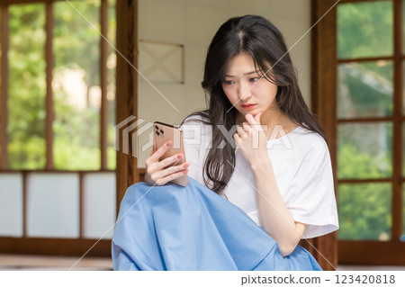 一位年輕女子在一棟老房子的陽台上歪著頭看著她的智慧型手機 123420818