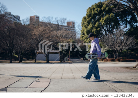 Skateboarder walking through the park with his skateboard Skateboarder walking through the park with his skateboard 123422343