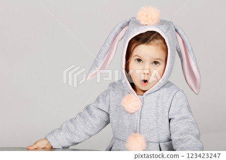Surprised Toddler in Bunny Costume Making Funny Expression on White Grey Background 123423247