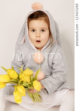 Surprised Toddler in Bunny Costume Holding Yellow Tulips on White Grey Background 123423269