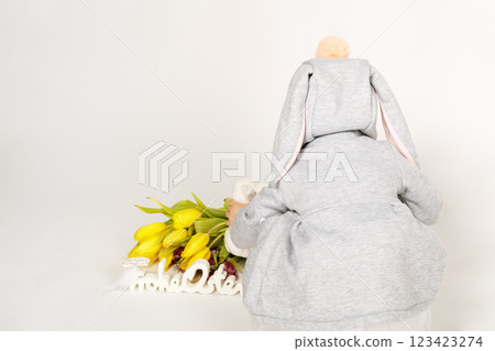 Toddler in Bunny Costume Sitting with Back to Camera and Yellow Tulips 123423274
