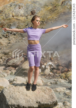 Female fitness model standing on rock in mountains against backdrop of steam and gases from geysers Female fitness model standing on rock in mountains against backdrop of steam and gases from geysers 123424143