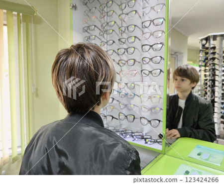 A young guy chooses glasses in an optics store, looks at the window to choose the perfect one. A young guy chooses glasses in an optics store, looks at the window to choose the perfect one. 123424266