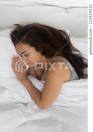 Peaceful Slumber: A woman peacefully sleeps in a bright bedroom, swathed in a white blanket atop her comfy orthopedic mattress.  123424532