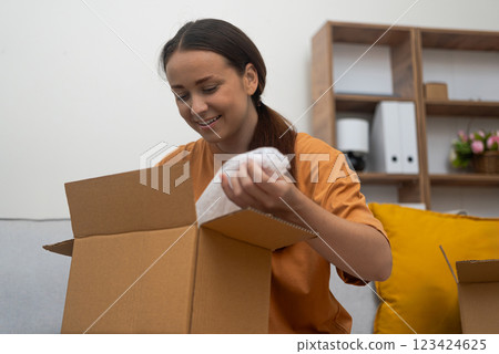 Seated, a woman's face lights up while she examines her delivered package, confirming her online purchase's success. 123424625