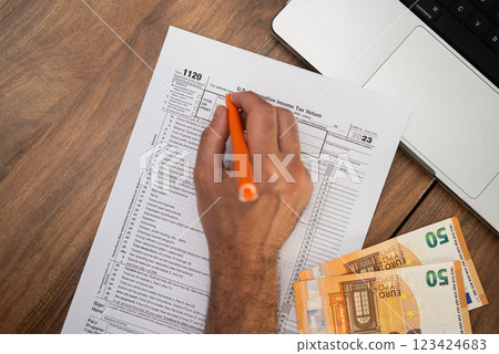 Filling out U.S. corporation income tax return form 1120 with euros on a wooden desk. Tax season, accounting, and financial planning concept  123424683
